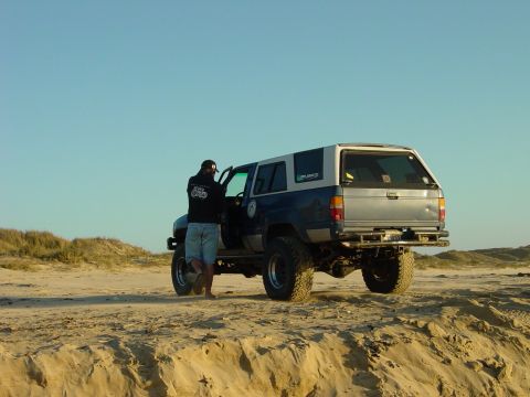 1999 Jeep Grand Cherokee - A person enters a modified SUV parked on a sand dune under a clear blue sky.