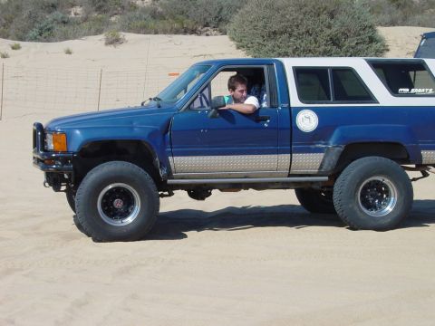 1999 Jeep Grand Cherokee - A blue and white pickup truck with a camper shell is seen from the side, with a person in the driver's seat.