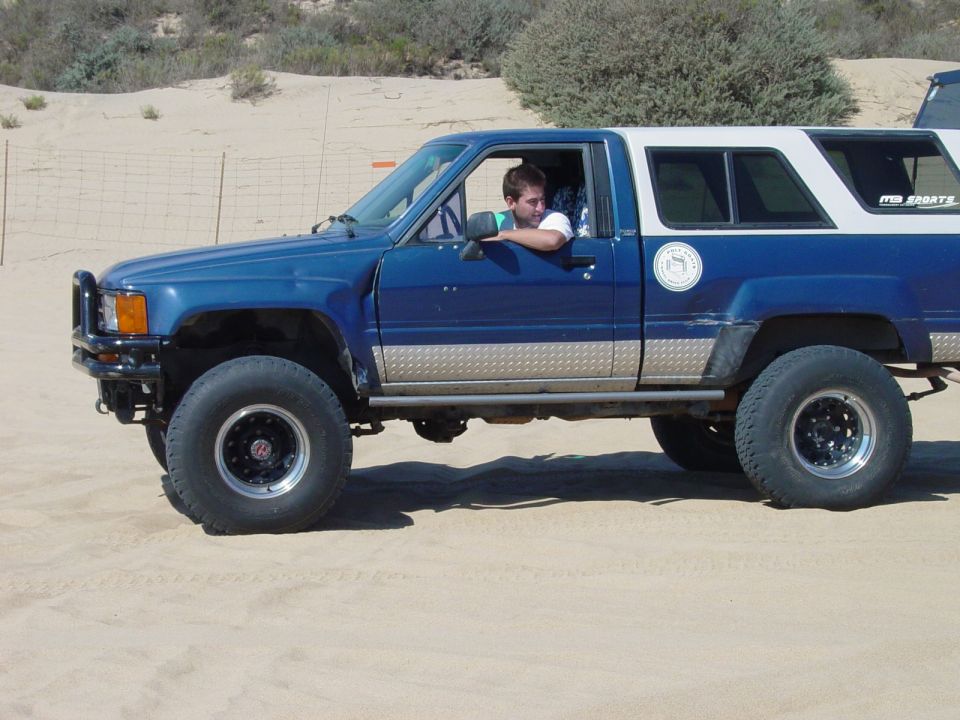 Blue and white pickup truck with camper shell, side view. Text on camper reads 'ITB SPORTS'