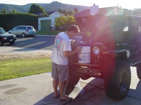 1999 Jeep Grand Cherokee - A man tends to a Jeep CJ-7 in a driveway, with other vehicles and houses in the background.