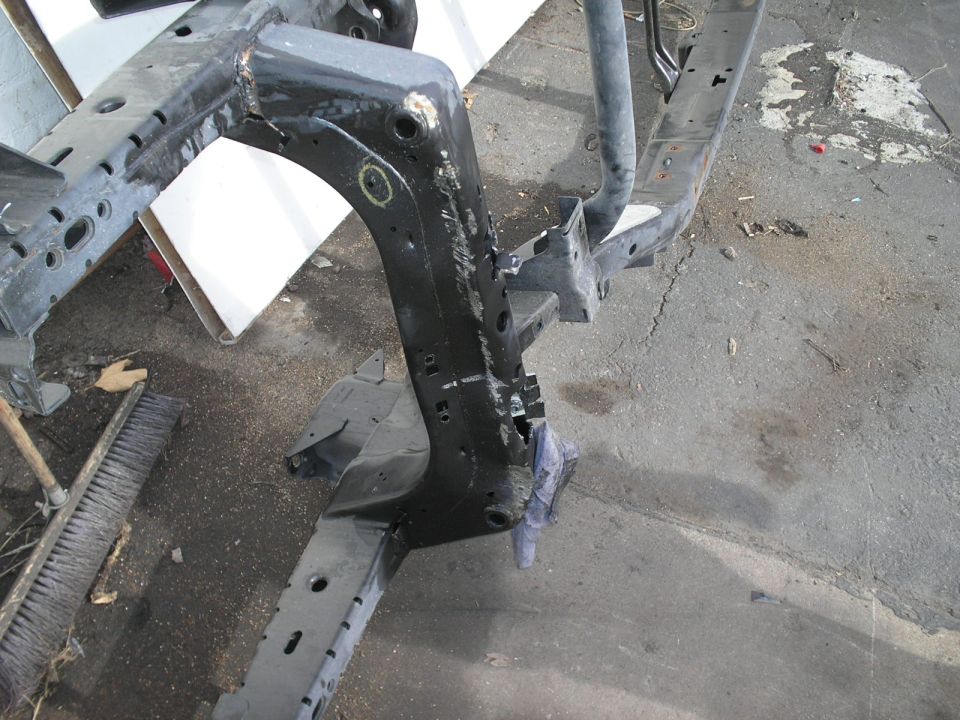 Close-up of a black metal vehicle frame with various mounting holes and welded sections. A blue cloth is draped over a section of the frame