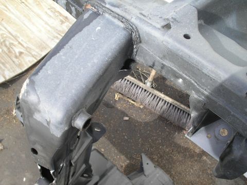1991 Ford Taurus - A close-up view of a vehicle's frame component, showing welds and structural details. A broom lies on the ground behind it.