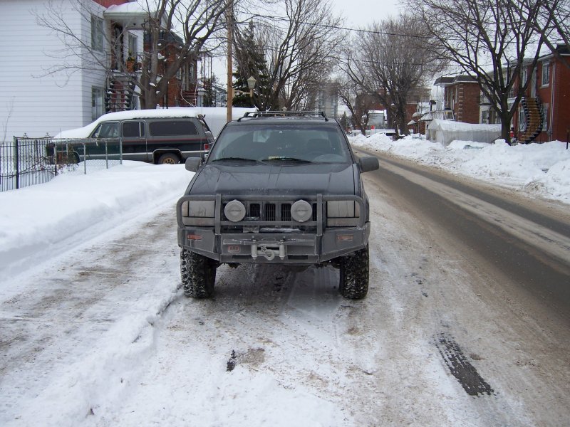 Front view of a 1996 Jeep Grand Cherokee with aftermarket bumper and winch in the snow
