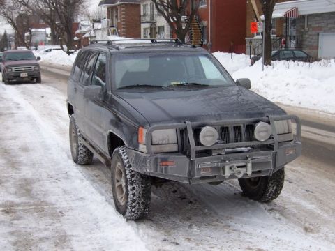 1996 Jeep Grand Cherokee - A dark-colored Jeep Grand Cherokee is parked on a snow-covered street with a brush guard and winch on the front.