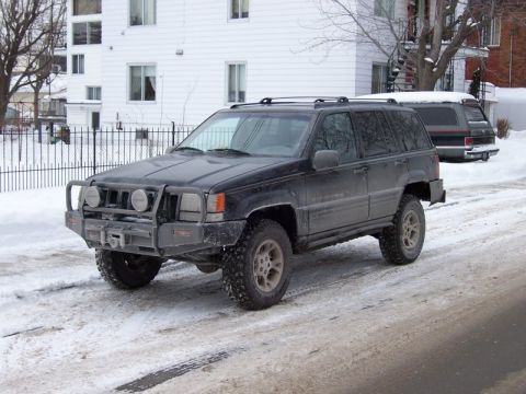 1996 Jeep Grand Cherokee - A black 1996 Jeep Grand Cherokee is parked on a snow-covered road in front of a building.