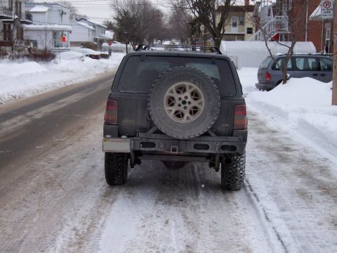 1996 Jeep Grand Cherokee - A Jeep Grand Cherokee sits on a snow-covered road, its spare tire prominently displayed on the rear.