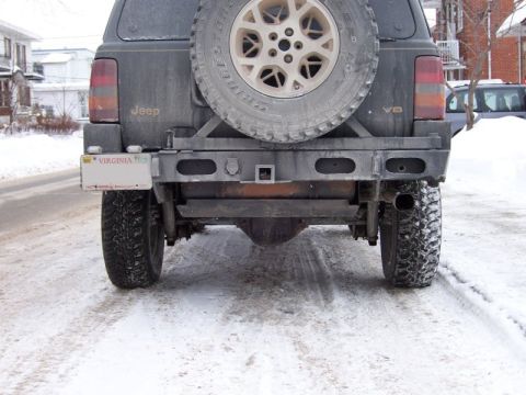1996 Jeep Grand Cherokee - The rear of a 1996 Jeep Grand Cherokee is shown in a snowy environment, displaying its spare tire and custom bumper.