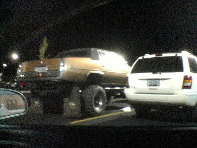Lifted gold sedan with oversized tires parked next to a white SUV