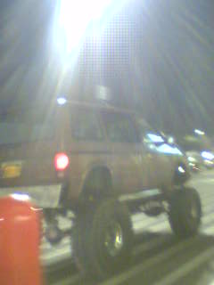 1994 Ford Probe - A heavily modified SUV with oversized tires is parked outdoors at night, illuminated by bright lights.