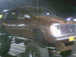 1994 Ford Probe - A modified brown van with an elevated chassis and oversized wheels is captured in a nighttime photograph.