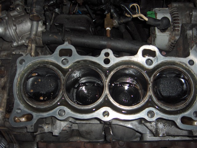 Four-cylinder engine block with head removed, showing pistons and head gasket