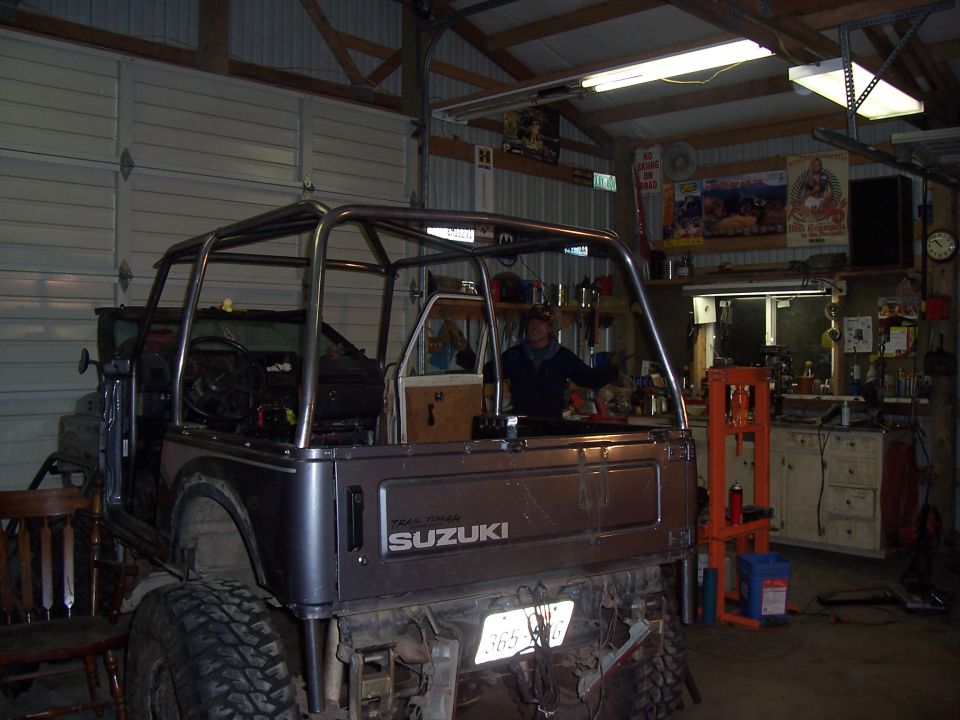 Suzuki Samurai with tube roll cage and tailgate up on jack stands inside metal pole barn shop