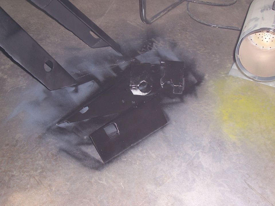 Freshly painted black steel frame brackets and bracketry on a concrete floor with overspray