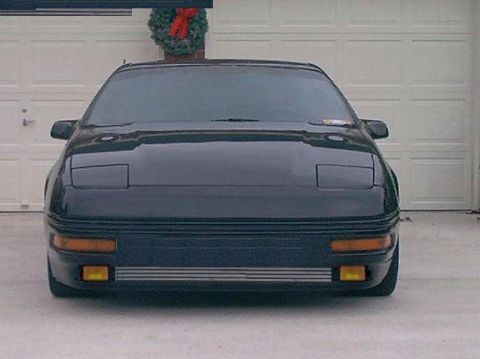 1996 Ford Probe - Front view of a dark coupe with pop-up headlights, parked in front of a garage door.