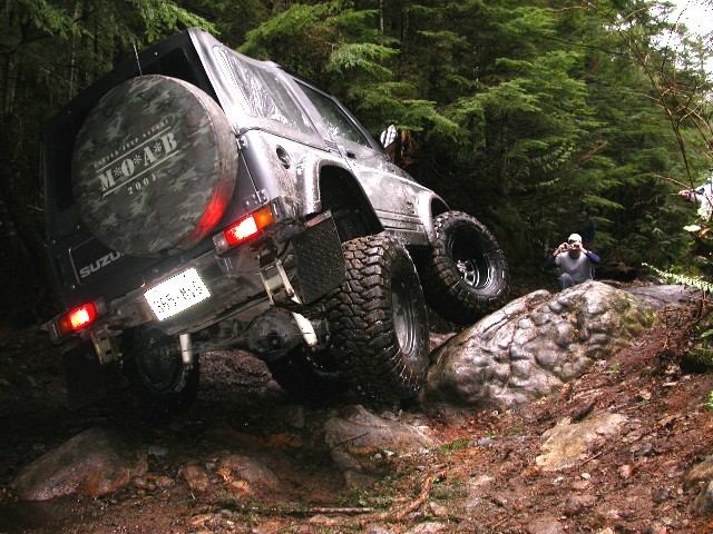 Rear view of lifted Suzuki Samurai climbing rocks with MOAB 2007 spare cover and brake lights on