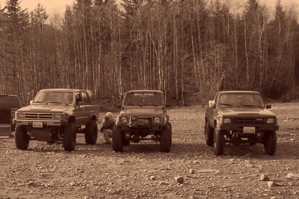 Three lifted mini trucks lined up on gravel in sepia tone, a Toyota pickup at each end