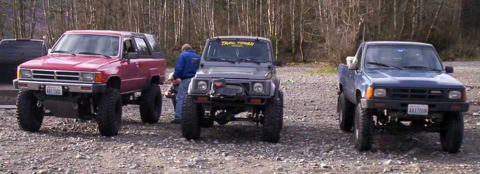 Red Toyota 4Runner, lifted Suzuki, and blue Toyota pickup parked side by side on gravel