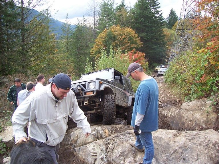 Recovered small 4x4 back upright on a rocky trail with several people standing around it
