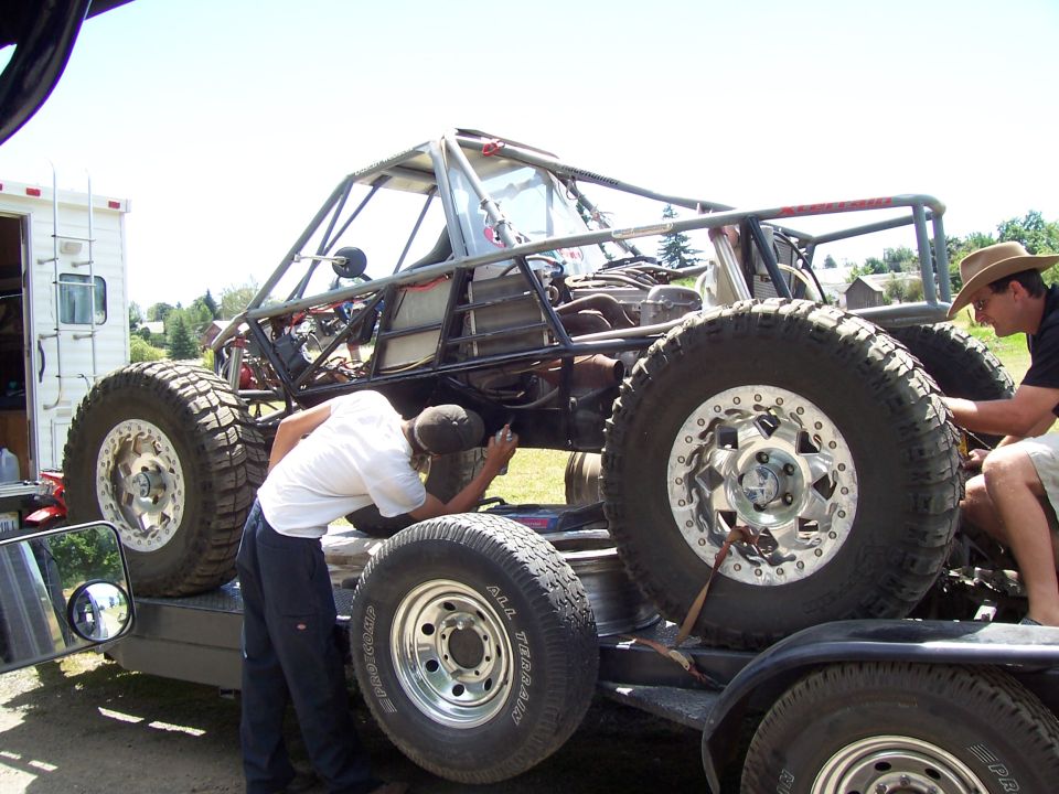 Tube-chassis rock buggy on a trailer with men working on it, beadlock wheels and big tires