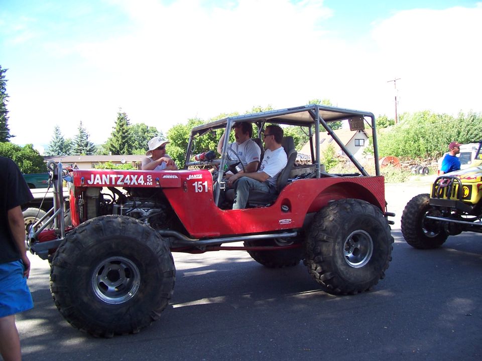 Red flatfender Jeep-style buggy marked JANTZ4X4 151 with people seated inside, driving on pavement