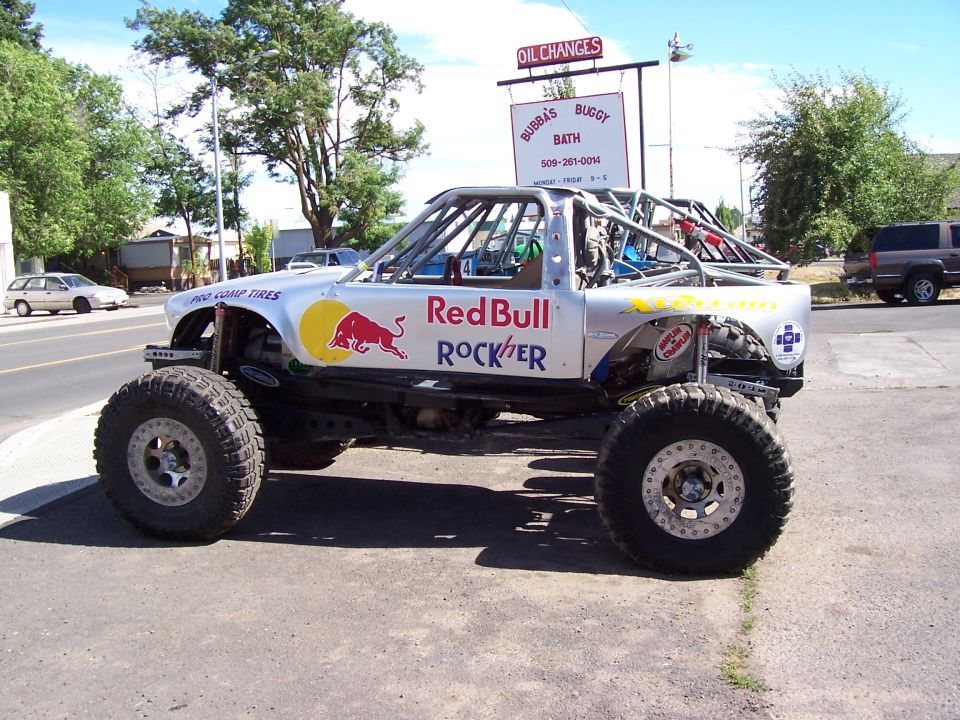 Silver Red Bull Rockher tube buggy parked on a street by an Oil Changes sign