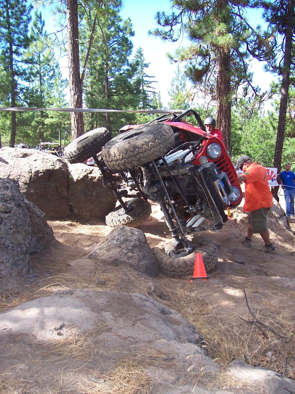 Red rock crawler tipped sideways against a boulder with orange cone nearby