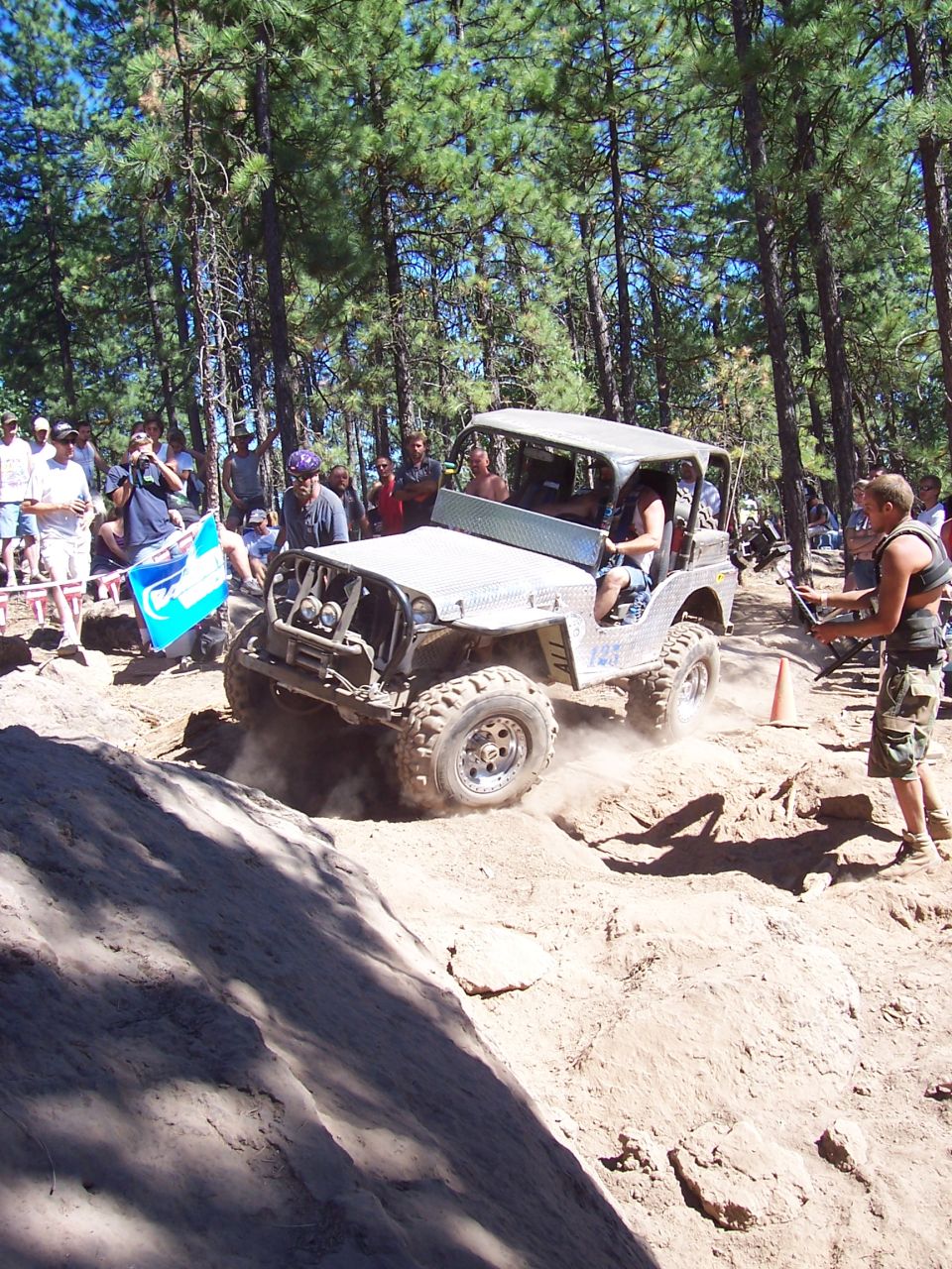 White flatfender-style Jeep number 1 throwing dirt as it climbs out of a dug-out section, spectators around