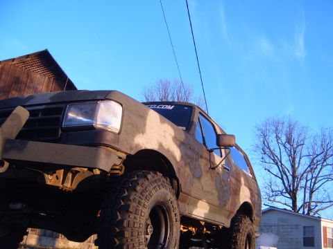 1988 Ford Bronco - Camouflaged 1988 Ford Bronco sits lifted under a clear blue sky.