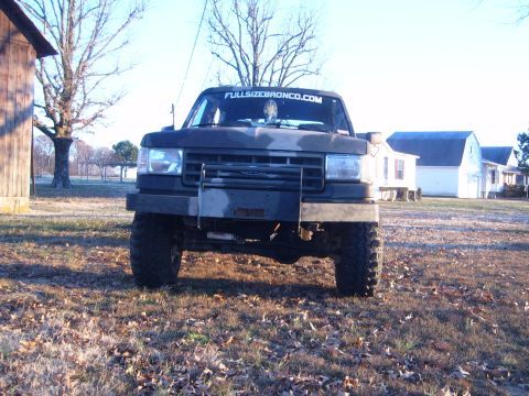 1988 Ford Bronco - This Ford Bronco is parked in a rural setting with houses and trees in the background.