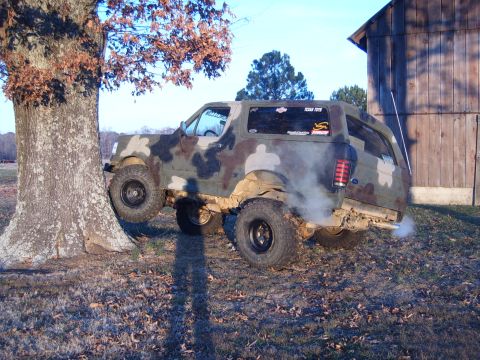1988 Ford Bronco - This camouflaged SUV appears to be stuck against a tree, with smoke coming from the exhaust.