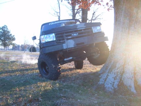 1988 Ford Bronco - 1988 Ford Bronco with camouflage paint is shown off-roading and climbing over a tree root.