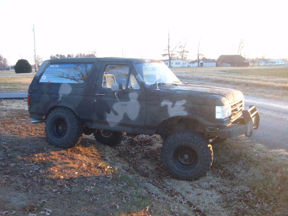 Camouflaged Ford Bronco with lifted suspension and off-road tires parked on a dirt incline