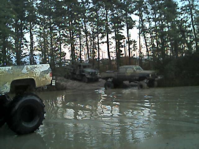 Lifted mud-covered 4x4 pickups around a flooded mud pit at dusk