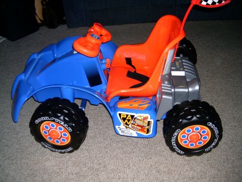 2006 Ford F1 - A blue and orange toy ride-on vehicle with flame decals and "Goodyear" tires sits on a carpeted floor.