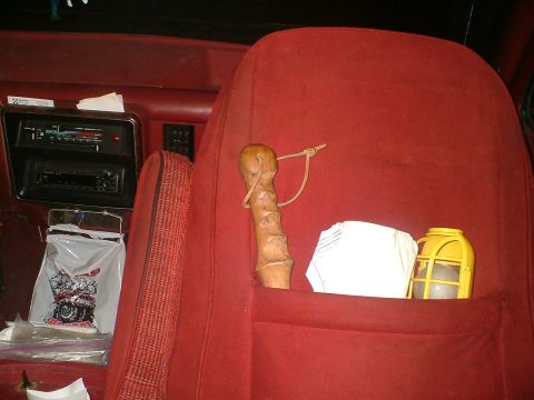 1989 Ford Bronco - The interior of a 1989 Ford Bronco features red upholstery, a dual-DIN radio, and a unique carved wooden item tucked into the seat pocket.