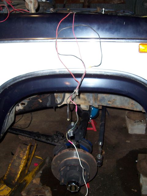 1983 Ford Bronco - The front suspension and wheel assembly of a white 1983 Ford Bronco is visible, with loose wiring hanging down.