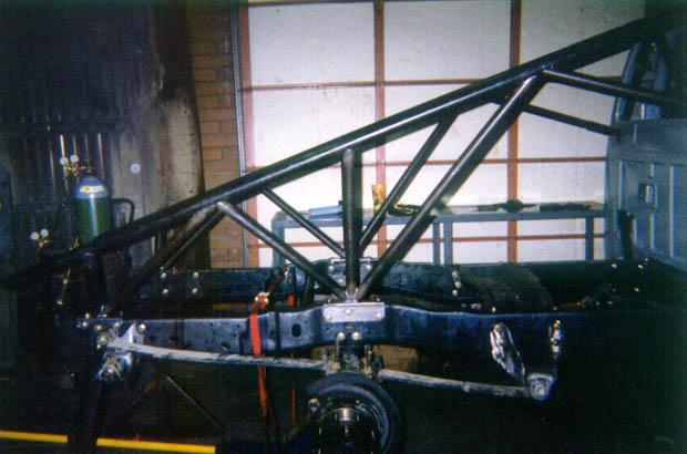 Truck chassis with custom roll cage being fabricated, showing suspension and frame components