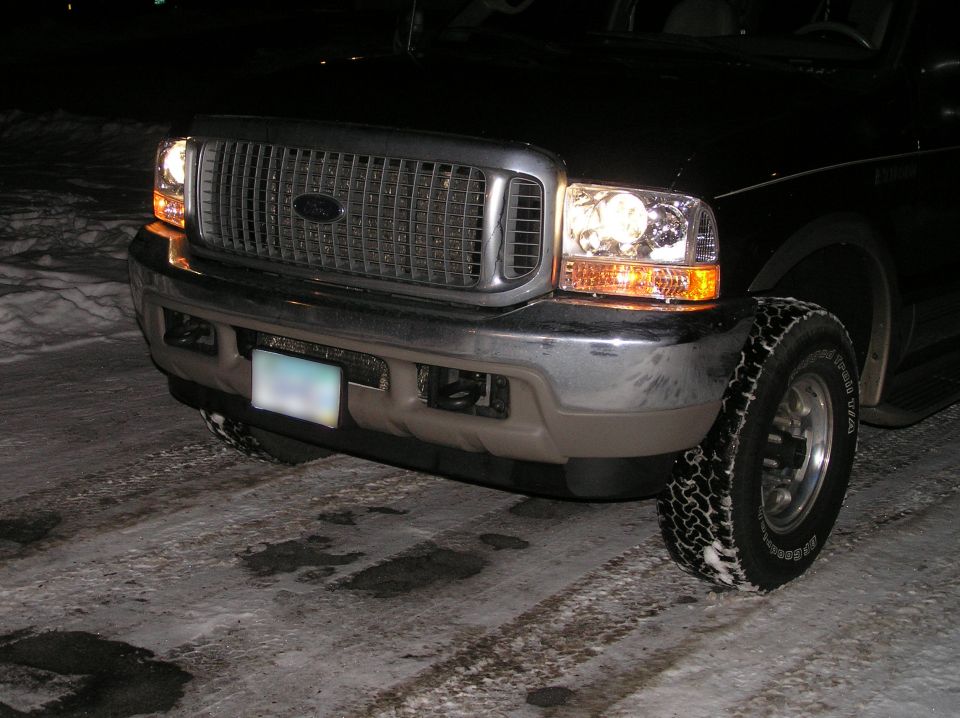 Black Ford Excursion front corner at night with lit headlights and amber turn signals on snowy pavement