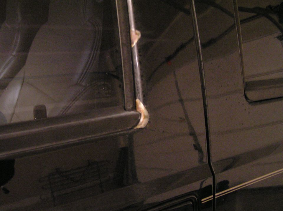 Night close-up of dark vehicle door frame corner with pale sealant on window trim