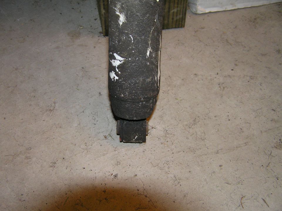 Dirty black vehicle part with white paint spots on concrete floor