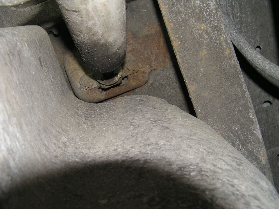 Underside close-up of rusty exhaust flange and bracket on cast-metal housing
