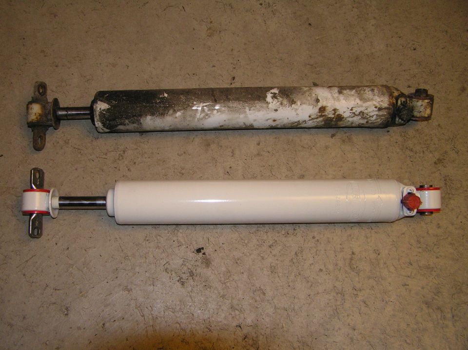 Old dirty shock absorber above a new white shock with red bushings on concrete