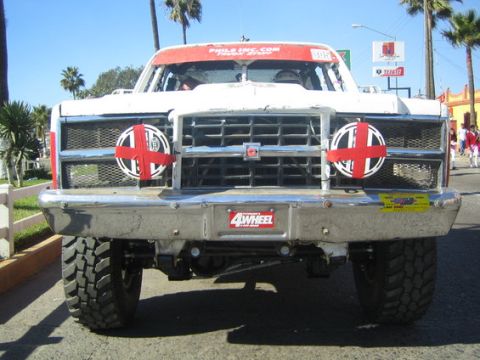1990 Ford Bronco - Head-on view of a white and red off-road race truck numbered 305, parked on a sunny palm-lined street with a chrome tube bumper.