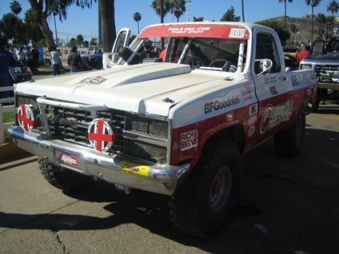 1990 Ford Bronco - Three-quarter front view of a white and red off-road race truck number 305 with BFGoodrich and California Tomatoes sponsor graphics at an o…