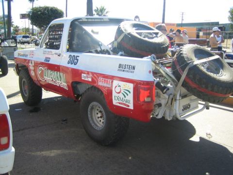 1990 Ford Bronco - Rear three-quarter view of a white and red off-road race truck number 305 with two spare tires and Bilstein and California Tomatoes graphic…