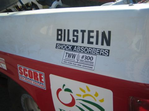 1990 Ford Bronco - Close-up of decals on a race truck panel reading Bilstein Shock Absorbers, TWW #300 Moji Brothers, and Score International Off-Road Racing.