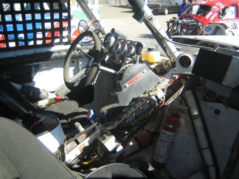 1990 Ford Bronco - Detailed interior of an off-road race truck showing a bare roll cage, suede steering wheel, gauge cluster, wiring and a mounted fire exting…