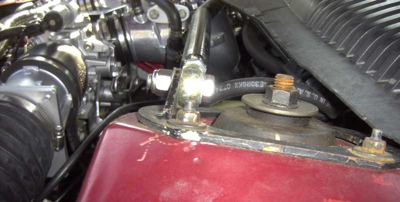 Red car engine bay with metal hoses and air intake assembly. Visible text: SUPERMOTORS.NET