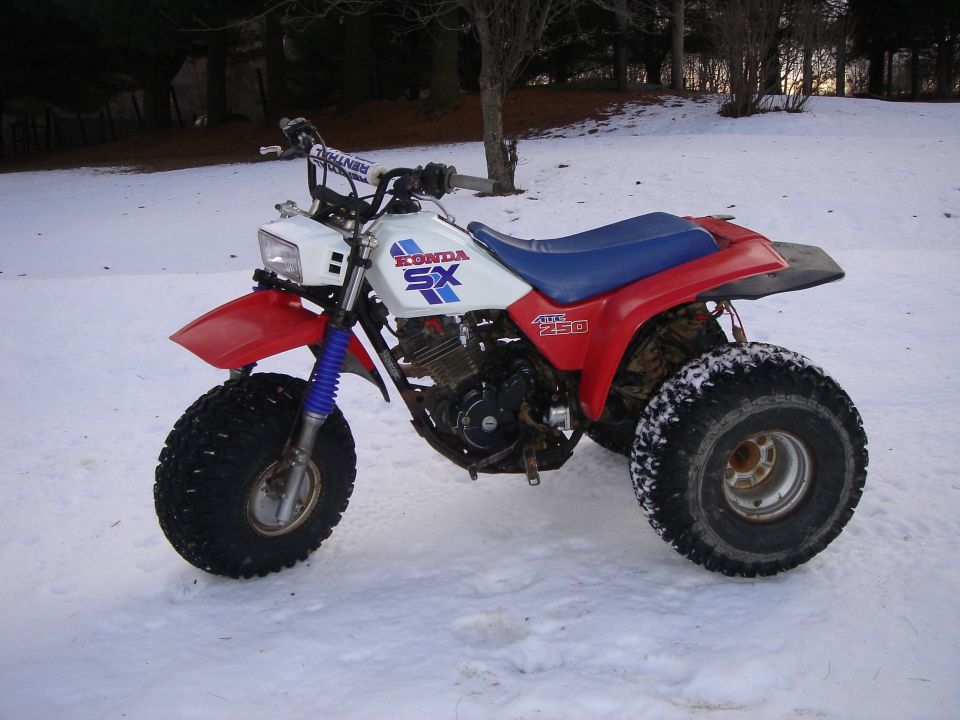 Red, white, blue Honda ATC 250 SX three-wheeler parked in snow, side view