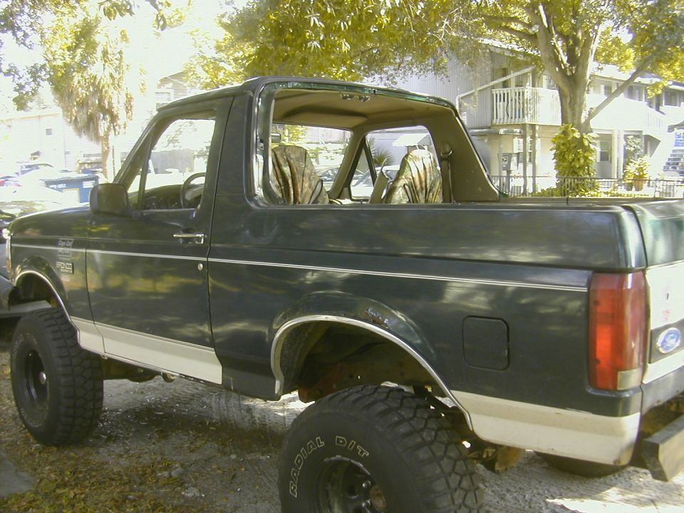 Green Ford Bronco with removed top, lifted on large mud tires in a parking lot